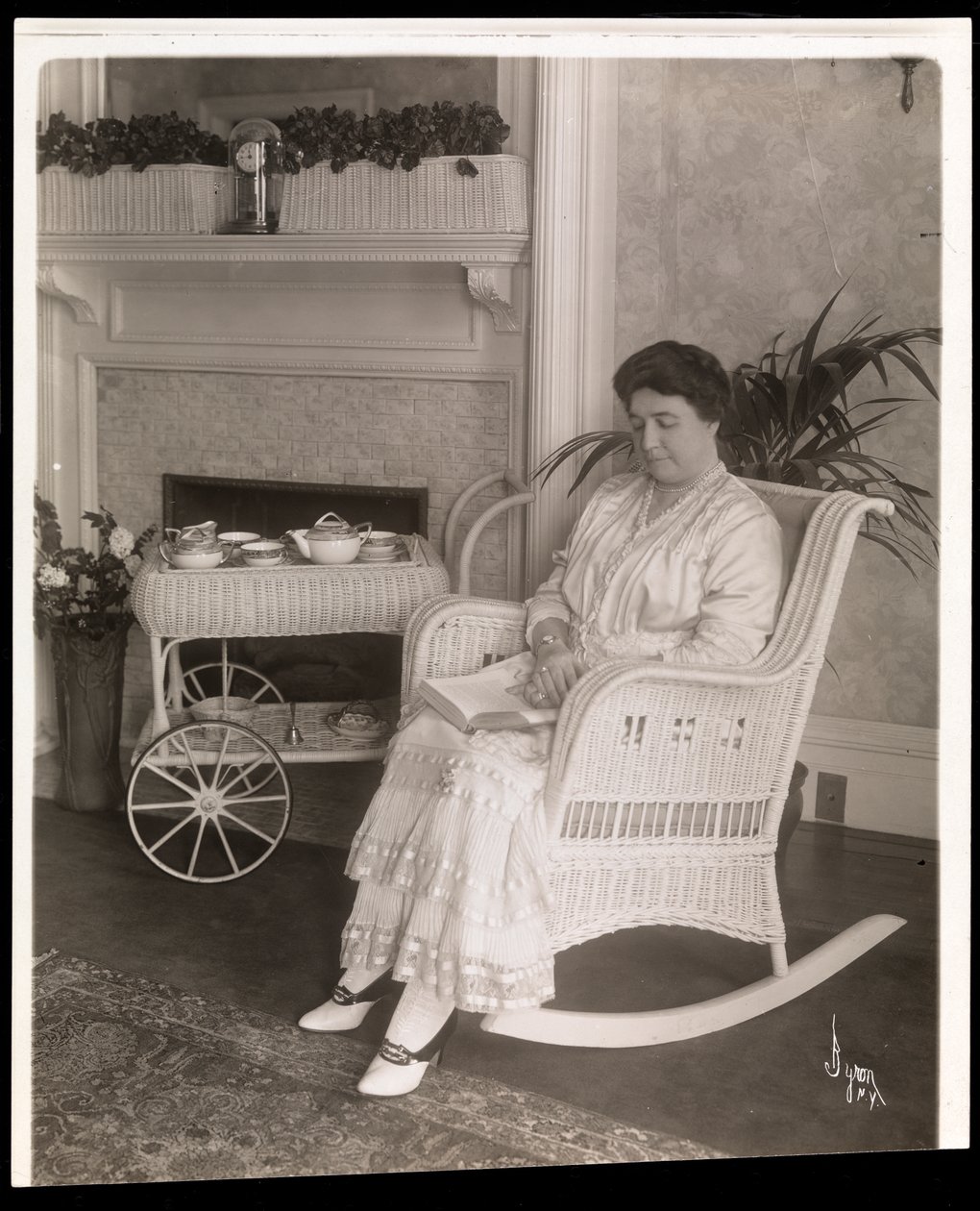 Mrs. Howard sitzt mit einem Buch in einem Schaukelstuhl in ihrem Haus in der 5th Avenue 200, New York, 1915-6 von Byron Company