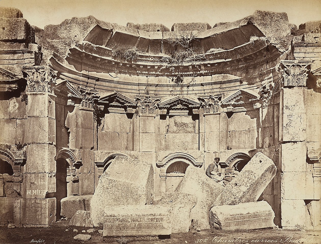 Detail der sogenannten "Räume" in der archäologischen Zone von Heliopolis oder Baalbek, antike syrische Stadt, jetzt Libanon. Ein Mann posiert, sitzend auf den Ruinen von Félix Bonfils