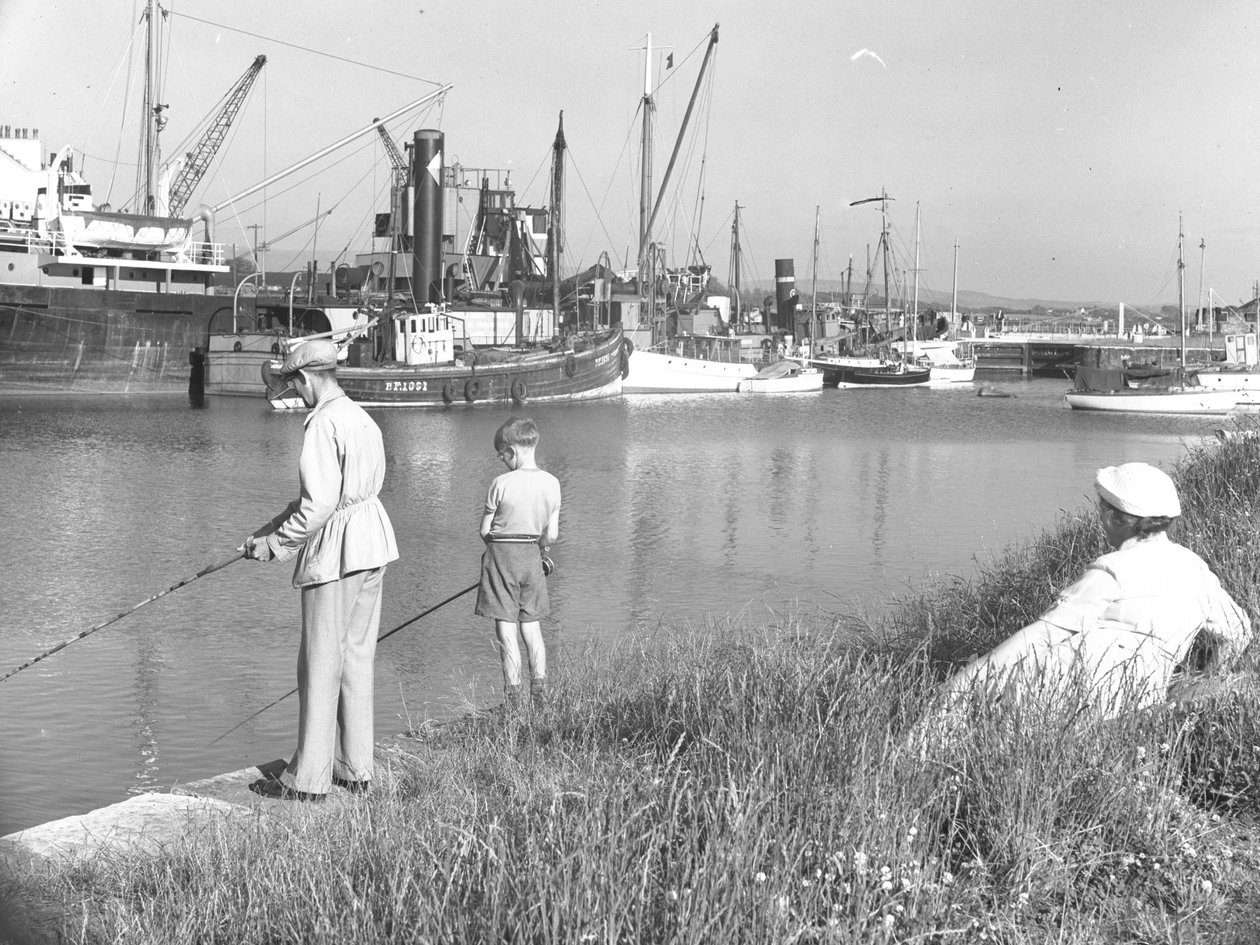Ein Mann und ein Junge angeln in Glasson Dock, während eine Frau im Hintergrund zusieht, verschiedene Boote vertäut von Joseph Hardman