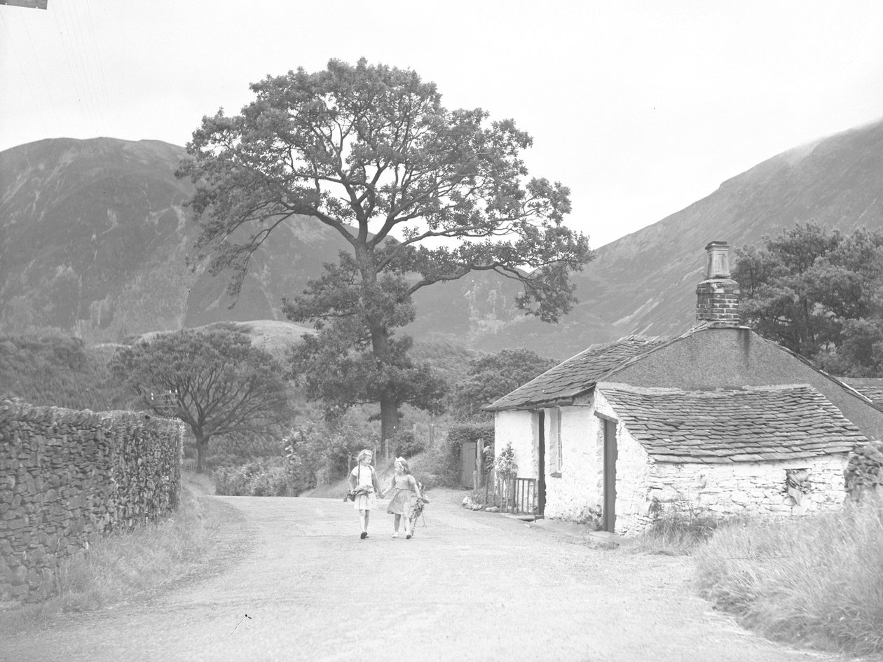 Zwei junge Mädchen halten sich an den Händen und tragen Fingerhüte, gehen die Straße entlang an einem Cottage vorbei zur Kamera von Joseph Hardman
