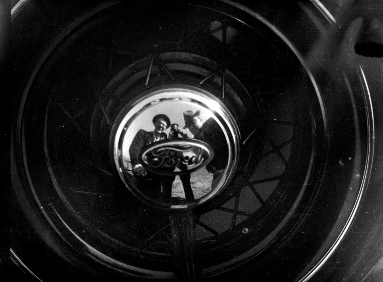Einige Menschen spiegeln sich in einer Ford-Radkappe von Luigi Leoni