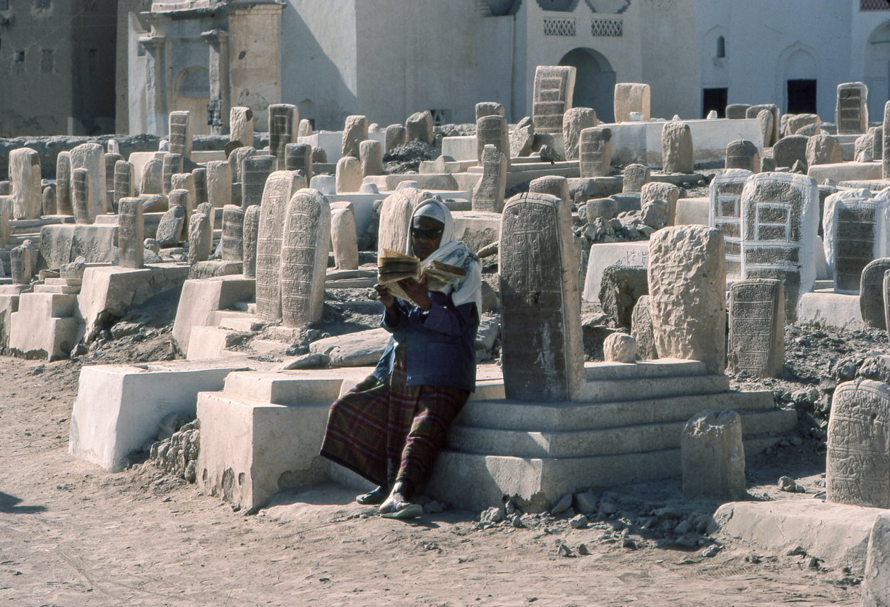 Ein jemenitischer Mann rezitiert den Koran auf einem Friedhof mit Gräbern in Sayun, Hadramaut, Südjemen. von Lynn Abercrombie