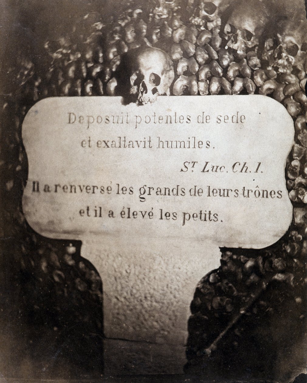 Die Beinhäuser der Katakomben von Paris. Peter trägt ein Zitat aus Kapitel 1 des Evangeliums von Lukas (Deposuit potentes de sede et exaltavit humiles. Auf Französisch: Er stürzte die Großen und erhob die Kleinen) von Nadar