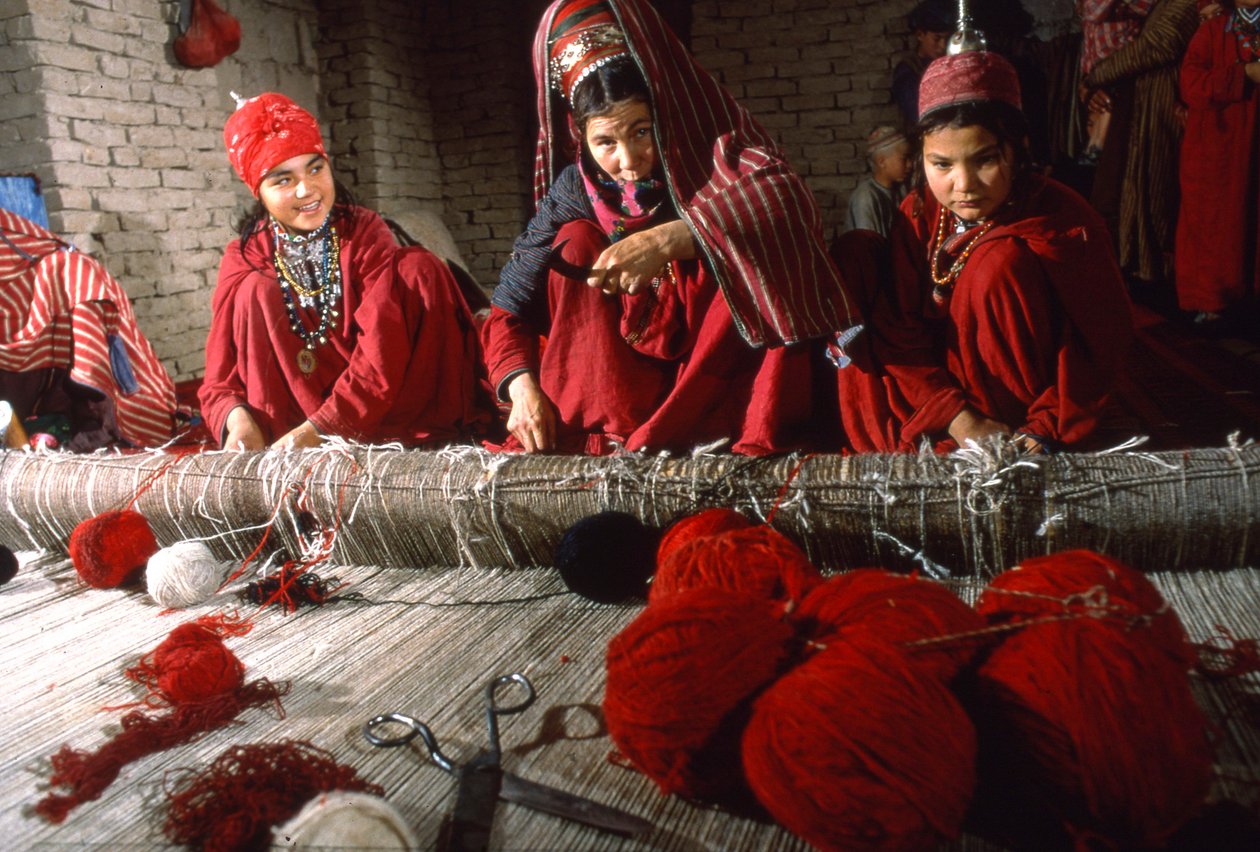 Turkmenische Stammesfrauen schneiden Knoten im Schuss eines Teppichs auf einem Webstuhl in einem Dorf von Thomas J. Abercrombie