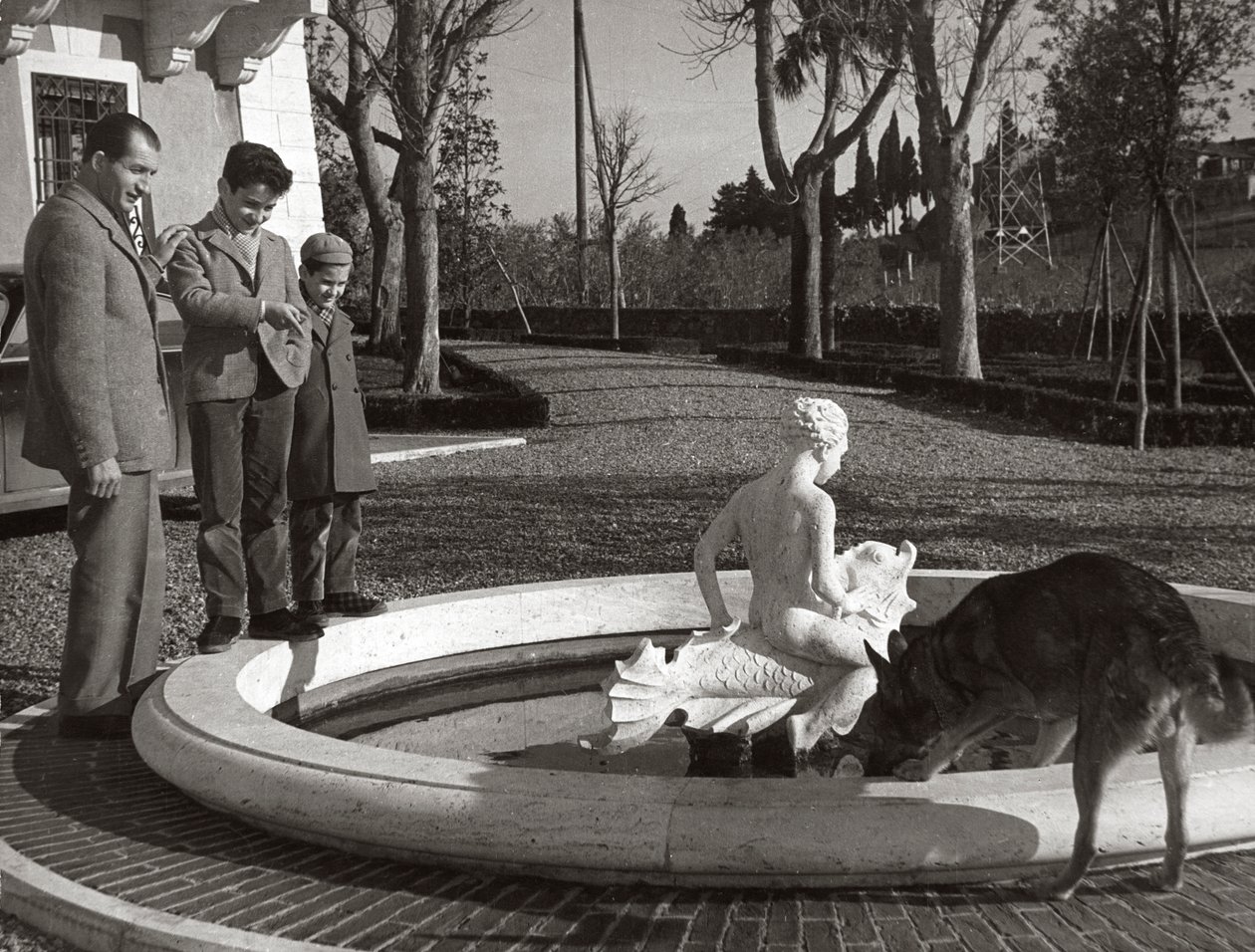 Gino Bartali mit zwei Kindern und einem Hund in der Nähe eines Brunnens von Unknown photographer