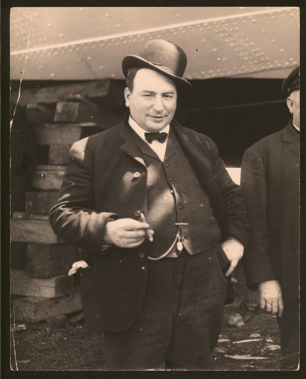 Vertikales Schwarz-Weiß-Foto eines Mannes mit Melone und Fliege, der eine Zigarre raucht von William G. Swekosky