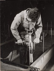 [Mann benutzt eine Handmaschine, um mit einem Stück Holz zu arbeiten] von Arnold Eagle