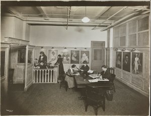 Hauptbüro/Empfangsraum bei der Mutual Film Co. mit Sekretärin am Schreibtisch, Menschen an einem Tisch beim Lesen und Porträts an der Wand, New York