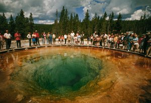 Parkbesucher versammeln sich um einen blau-grünen, blütenförmigen Thermalpool. Yellowstone Nati...