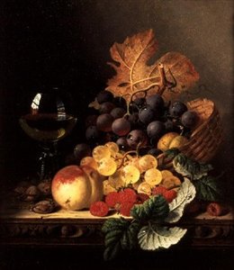 Ein Korb mit Trauben, Himbeeren, einem Pfirsich und einem Weinglas auf einem Tisch