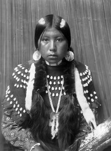 Kalispel-Indianerin, weiße Streifen auf dem Haar gemalt, Muschelscheiben-Ohrringe, trägt ein mit Elchzähnen verziertes Decken-Kleid, ca. 1910, Foto von Edward S. Curtis