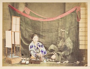 Japanisches Paar in ihrer Freizeit, Studio-Tableau einer jungen japanischen Frau, die mit Teezubehör um sich herum sitzt und eine Pfeife an eine männliche Figur hinter ihr reicht, die von einem Leinen-Moskitonetz abgeschirmt ist, Fotograf: Unbekannt, Lucas von English Photographer