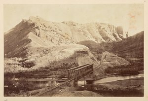 Ansichten der Pazifikbahn, Eisenbahnschienen, die einen Fluss auf einer Fachwerkbrücke überqueren, mit Bergen dahinter