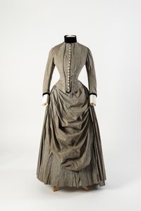Graues Baumwollkleid mit drapiertem Schürzenfront und schwarzem Samtbesatz am Kragen und an den Manschetten, späte 1880er Jahre
