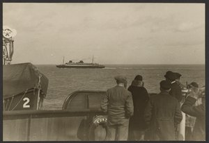 Gruppe von Menschen auf dem Deck eines Schiffes, die ein anderes vorbeifahrendes Schiff beobachten