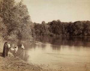 Ein Mann in traditioneller Kleidung mit seinem Pferd vor einem See in Ägypten