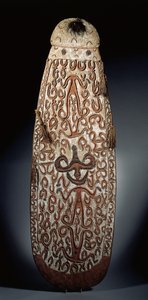 Ovaler Asmat-Schild, reliefartig geschnitzt mit scrollenden Ornamenten, die stark stilisierte Figuren einbeziehen, geflochtene Quasten am Rand