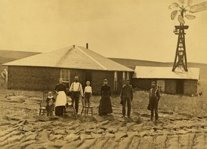 Familie von Siedlern vor ihrem Sodenhaus mit einer Windmühle auf dem Dach des angrenzenden Gebäudes in Custer County, Nebraska, ca. 1885