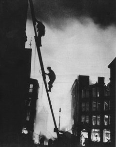 Im Blitz, silhouettiert gegen das Licht der Feuer, klettern Rettungsmänner in ein Gebäude in St.