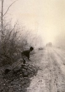 Eine Landstraße in Morgennebel gehüllt. Im Vordergrund spaltet ein Mann Steine