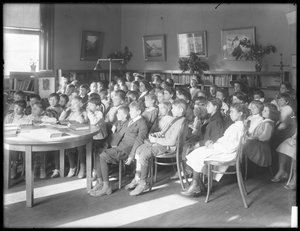 Kinder sitzen und hören im Lesesaal einer nicht identifizierten Filiale der Queens Borough Public Library zu, ca. 1910