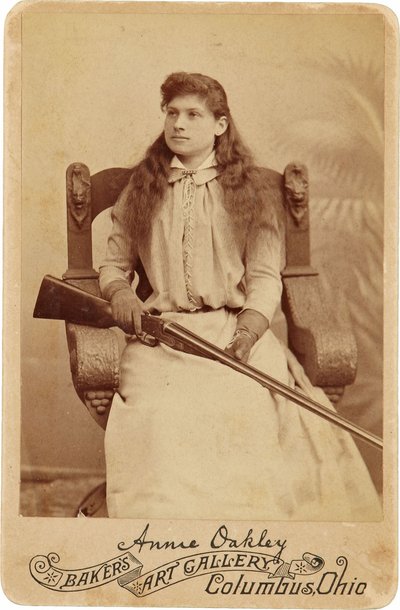 Annie Oakley: Hier sitzt die legendäre Scharfschützin eher schüchtern in einem massiven Renaissance-Stil Stuhl, ein Gewehr ruht auf ihrem Schoß. Ihre zarten weiblichen Züge und fließenden Haare täuschen über ihr robustes Outdoor-Image hinweg von American Photographer