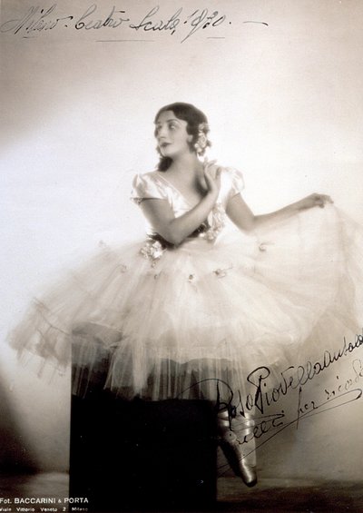 Porträt der klassischen Ballerina Rosa Piovella Ansaldo, im Tutu und Ballettschuhen. Sie sitzt frontal, ihr Gesicht zur Seite gedreht. Stoffrosen schmücken ihr Kleid und sorgfältig frisiertes Haar (Mailand, Teatro alla Scala) von Baccarini and Porta
