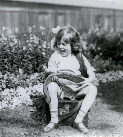 Ein junges Mädchen, Betty, hält eine östliche Indigo-Schlange, während sie auf einem Lederkoffer sitzt, Londoner Zoo, 1924 von Frederick William Bond
