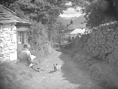 Eine Frau sitzt lesend mit einem Hund in einer Gasse von Joseph Hardman
