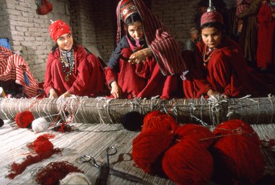 Turkmenische Stammesfrauen schneiden Knoten im Schuss eines Teppichs auf einem Webstuhl in einem Dorf von Thomas J. Abercrombie