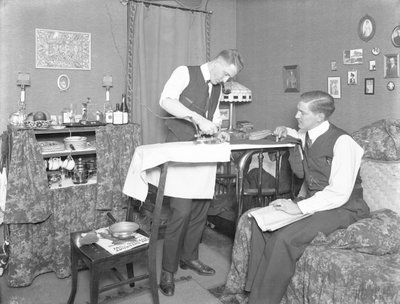 Unidentifizierter Mann, der die Verwendung eines elektrischen Bügeleisens demonstriert, beobachtet von einem anderen Mann, ca. 1913-14 von William Davis Hassler