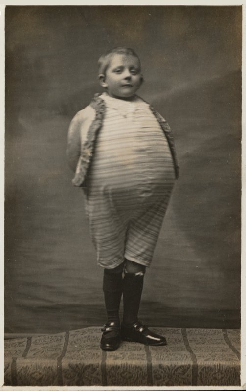 Schuljunge, verkleidet mit einem sehr großen Bauch (s/w Foto) von English Photographer