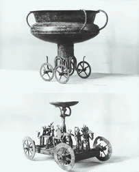 Zwei Votivwagen zum Sammeln von Regenwasser: Oben - Tasse auf vier Rädern aus dem Peccatel-Hügel, Mecklenburg, Deutschland. Unten - stehende weibliche Gottheit unter einem Teller umgeben von Kriegern