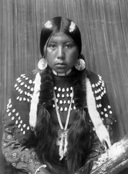 Kalispel-Indianerin, weiße Streifen auf dem Haar gemalt, Muschelscheiben-Ohrringe, trägt ein mit Elchzähnen verziertes Decken-Kleid, ca. 1910, Foto von Edward S. Curtis