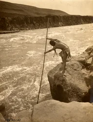 Tlakluit-Indianer, stehend auf Felsen, fischend mit Dip-Netz, ca. 1910 (s/w Foto)