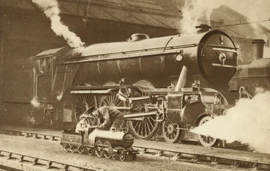 Junge reitet auf einer Spielzeug-Dampflokomotive vor dem echten Ding (s/w Foto)