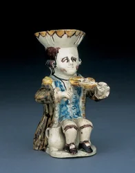 Toby-Krug eines Fiedlers, sein Hut mit braun-gelb gebogtem Rand, sein braunes Haar eingeritzt und mit einer weißen Rosette zum Zopf gebunden, in einem braun lavierten Gehrock, ca. 1770