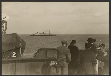 Gruppe von Menschen auf dem Deck eines Schiffes, die ein anderes vorbeifahrendes Schiff beobachten