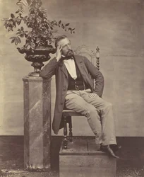 Mathias Höusermann, sitzend mit Ellbogen auf Sockel, hält eine Vase mit Blumen