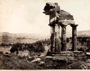 Ansicht der verbleibenden vier Säulen, die ein Gebälk des Tempels von Castor und Pollux im Valle dei Templi, Agrigent, tragen. Im Hintergrund ist ein Panorama der Stadt sichtbar
