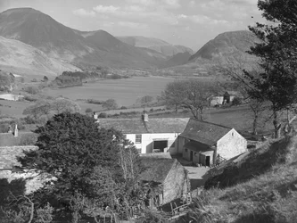 Blick auf einen Bauernhof im Vordergrund und einen See und Hügel im Hintergrund