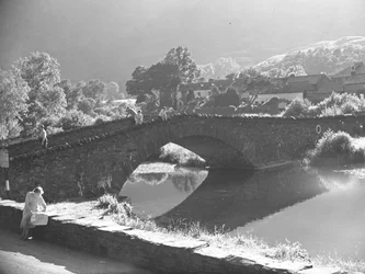 Frau sitzt auf einer Mauer und studiert eine Karte mit Fluss und Steinbrücke im Hintergrund