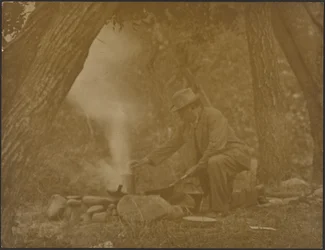 [Mann kocht am Lagerfeuer im Wald]
