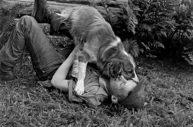 Junger Mann spielt mit seinem Hund vor ihrer Blockhütte in Palmer, Alaska