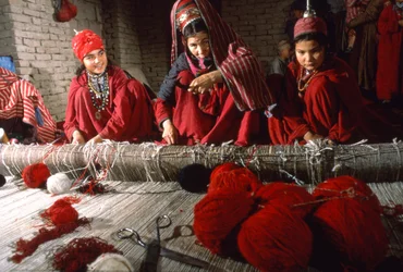 Turkmenische Stammesfrauen schneiden Knoten im Schuss eines Teppichs auf einem Webstuhl in einem Dorf