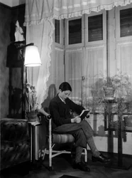 Ein Teenager sitzt in einem bürgerlichen Interieur und liest ein Buch, trägt kurze Hosen und hohe Socken. 1915. Historisches Foto, Frau liest, ca. 1915.