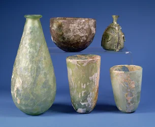 Im Uhrzeigersinn von links: birnenförmige grüne Glasflasche, Sassanidisch, 3.-7. Jahrhundert n. Chr.; hellbernsteinfarbene Glasschale, Sassanidisch, 5.-6. Jahrhundert n. Chr.; islamische grüne Glasbirnenflasche, ca. 8.-12. Jahrhundert n. Chr.; zwei islamis