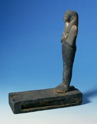 Ptah-Sokar-Osiris-Figur mit dreiteiliger Perücke und gekreuzten Armen auf einem rechteckigen Sockel mit einem Fach, das einen Abschnitt von Papyrus enthält, Ägyptisch, 21.-22. Dynastie, ca. 900 v. Chr.
