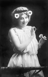Frau zupft Blütenblätter von einer Blume: „Er liebt mich. Er liebt mich nicht. Er liebt mich...“ Fotografie um 1912