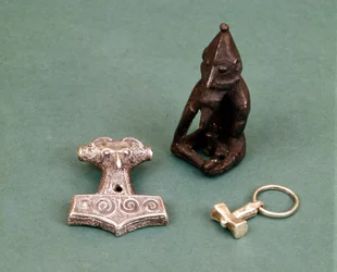 Amulette der Wikinger-Gottheiten: Im Vordergrund zwei kleine Silberhämmer, die den Gott Thor symbolisieren. Die Statuette stellt Freyr, den Fruchtbarkeitsgott, dar. Historisches Museum Stockholm, Schweden.